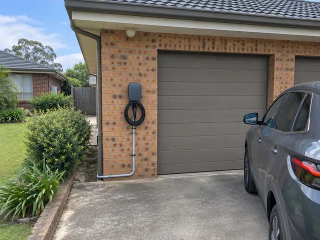 Wall-mounted EV charger on a brick garage wall beside a driveway and parked SUV in Thornton